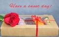 Red rose and a box of cakes tied with a red gift ribbon on a gray background