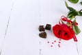 Red rose, chocolates on a white wooden background