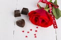 Red rose, chocolates on a white wooden background