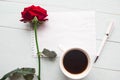 Red rose, coffee cup and white mockup blank on wooden background.