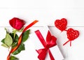 Red rose, gift with red ribbon, two red decorative hearts on the white wooden background. Women`s day, mother day, valentines day Royalty Free Stock Photo