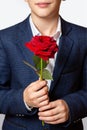 Red rose in the hands of a teenager. The boy is dressed in a blue suit and white shirt