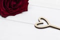 Hollow wooden heart on white wooden background. Red rose in the background. Valentine`s day or Love concept. Royalty Free Stock Photo