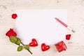 A red rose, two decorative hearts and a gift box lie on a table with a white sheet of paper and pen. Mockup for Royalty Free Stock Photo