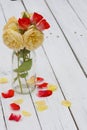 Red and yellow Roses glass bottle on wooden table with petals Royalty Free Stock Photo