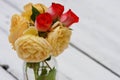 Red and yellow Roses in vase on wooden table with petals Royalty Free Stock Photo