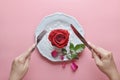 Red rose on white dish, with hand holding fork and knife, On pink background, Concept of Valentine`s Day. Royalty Free Stock Photo