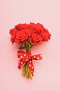Red roses bouquet decorated with ribbon on a pink background.