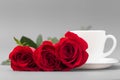 Red roses with a coffee cup of white color on a gray background Royalty Free Stock Photo