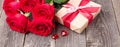 Red roses flowers and gift box on gray wooden table. Greeting card. Copy space for text. Horizontal banner Royalty Free Stock Photo