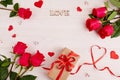 Red roses, a gift box made of craft paper with a red ribbon, the inscription love on a white wooden background. Royalty Free Stock Photo