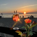 red roses and glass of orange  water  with ice  on wooden table top    sunset at sea  in beach restaurant view in pink sky and se Royalty Free Stock Photo