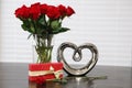 Red roses in glass vase with water and one rose next to vase gift and silver heart Royalty Free Stock Photo