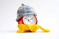 Red round alarm clock in knitted wool blue hat and yellow scarf on a white background. winter time concept. winter season Royalty Free Stock Photo