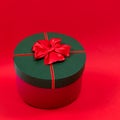 Red round gift box with a red bow on a green lid on a red background. Side view. Royalty Free Stock Photo