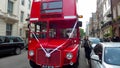 A red Routemaster bus on a London street with ribbon wedding celebration.