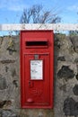 Red Royal Mail postbox on stone wall with blue sky background Royalty Free Stock Photo