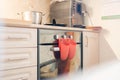 Red rubber kitchen mittens. Hang on an induction cooker. It also has a pan and a frying pan. Coffee machine on the background, on Royalty Free Stock Photo