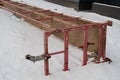 Red rusty construction cradle lies on its side in the snow next to the foundation of the house, background