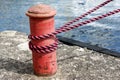 Red sailing hawser mooring rope from yacht in the port on concrete quay Royalty Free Stock Photo