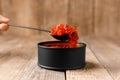 Red salmon caviar in a black tin can and a black spoon full of caviar on a wooden background Royalty Free Stock Photo