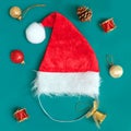 Red Santa hat with cute small colorful ornaments toys baubles around on green background flay lay. Winter Christmas New Year
