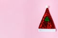 Red Santa hat decorated with sparkles with a green Christmas tree in the center on a pink background. Copy space for