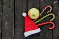 Red Santa hat, one apple, three candy cane lollipops on dark brown wood background Royalty Free Stock Photo