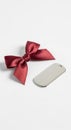 A red satin bow lies next to a shiny, rectangular silver dog tag with a rounded top and a hole at Royalty Free Stock Photo