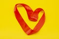 Red satin ribbon in the shape of a heart on a yellow background. Valentine`s Day Royalty Free Stock Photo