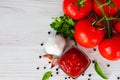 Red sauce or ketchup in a glass bowl, tomatoes, garlic, basil, parsley, black pepper on a wooden white background. Royalty Free Stock Photo