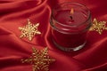 A red scented candle with Christmas star ornaments on a bright red silk cloth background Royalty Free Stock Photo