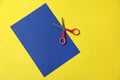Red scissors and blue paper on yellow background, top view. Space for text Royalty Free Stock Photo