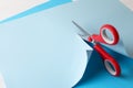 Red scissors cutting light blue paper on white background, closeup Royalty Free Stock Photo