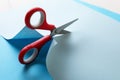 Red scissors cutting light blue paper on white background, closeup Royalty Free Stock Photo