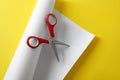 Red scissors and white paper on yellow background, top view Royalty Free Stock Photo