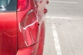 Red scratched car with damaged paint in crash accident or parking lot and dented damage of metal body from collision