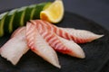 Red sea bream sashimi with cucumber and lemon slices on dark woo