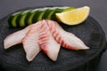 Red sea bream sashimi with cucumber and lemon slices on dark woo