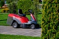 A red self-driving lawn mower stands without a driver in the Park. Mowing grass in the Park with a self-propelled lawn mower