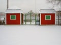 Red shed with a green shuttered door in a wintery landscape covered in white snow