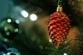 Red shining pine acorn cone hanging on a Christmas tree with blur bokeh background. New Year decoration prop.