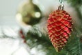 Red shining pine acorn cone hanging on a Christmas tree with blur bokeh background. New Year decoration prop.