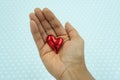 Red shiny heart in the palm of mixed race woman at white dotted blue background. Royalty Free Stock Photo