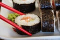 Red shopsticks holds maki sushi