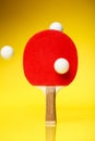 Red side of a ping pong racket with three white balls in the air, standing on a yellow background Royalty Free Stock Photo