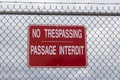 Red sign on a chain link fence saying No Trespassing in english and french language Royalty Free Stock Photo