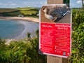 A red sign fixed to a wooden post on the Pembrokeshire Coast Path warns of avian flu and advises on precautions and actions