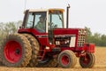 A red six wheel International 1586 tractor with cabin is plowing a blank agricultural field Royalty Free Stock Photo