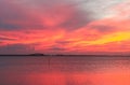 Red sky and ocean near end of stunning sunset with purple and yellow streaks and cars going over bridge and lights of shore in dis Royalty Free Stock Photo